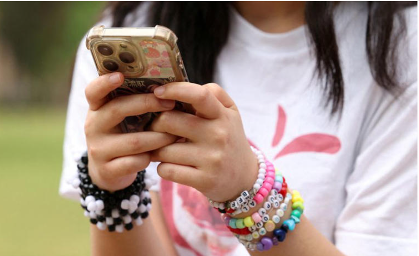 Australia cấm trẻ em dưới 16 tuổi sử dụng mạng xã hội- Ảnh 1. A person holding a phone AI-generated content may be incorrect.