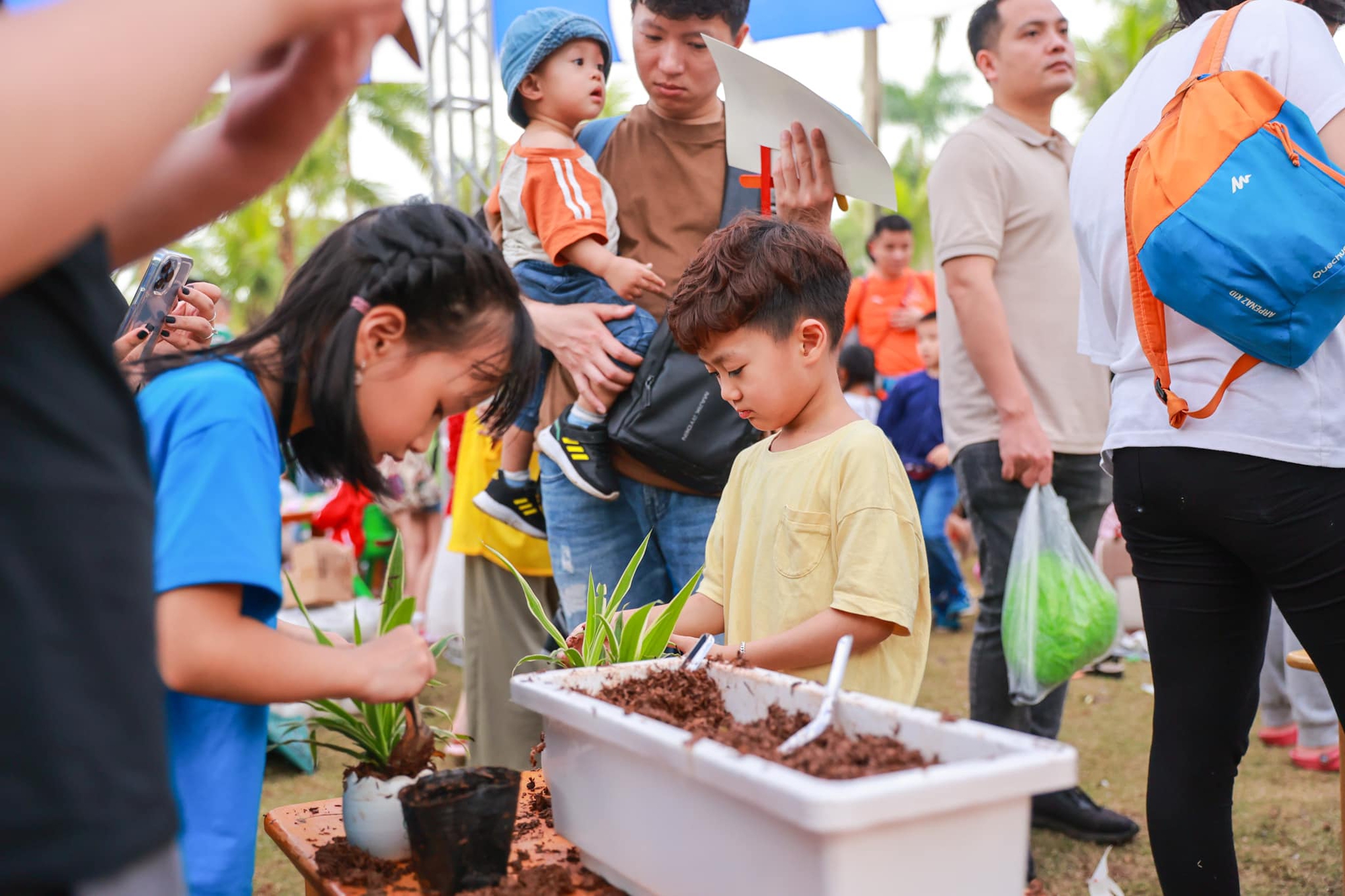 Giải phóng đôi chân, trải nghiệm mùa hè rực rỡ tại “Lễ hội mùa hè Eco Central Park 2025”- Ảnh 6. A group of people standing around a planter Description automatically generated