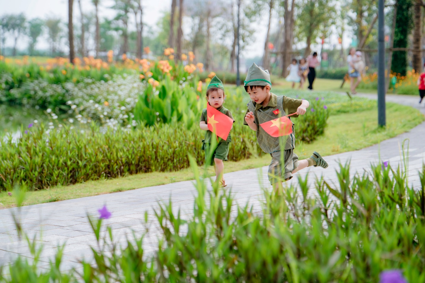Giải phóng đôi chân, trải nghiệm mùa hè rực rỡ tại “Lễ hội mùa hè Eco Central Park 2025”- Ảnh 8. Two children running on a path with flags Description automatically generated