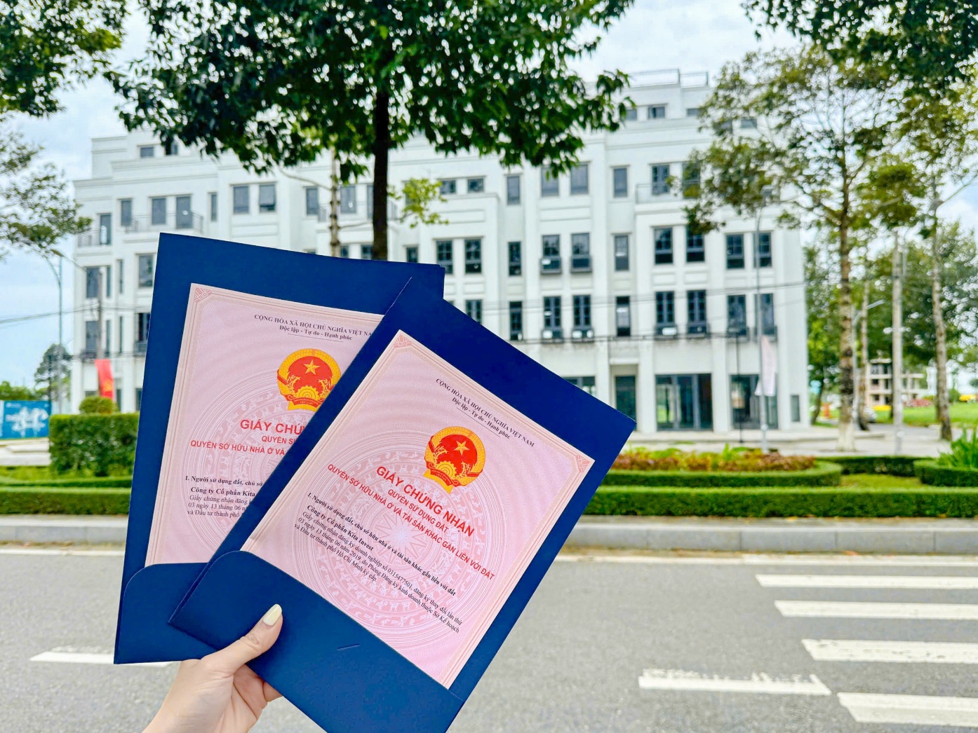 KITA Airport City bàn giao sổ hồng, khẳng định cam kết pháp lý tường minh- Ảnh 1. A hand holding a pair of blue papers AI-generated content may be incorrect.
