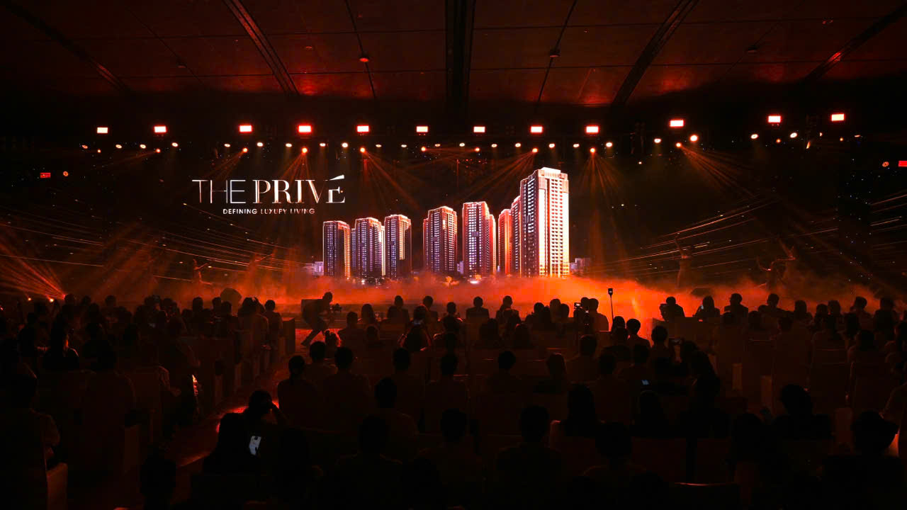 A group of people in a room with a stage with lights and a stage with a building in the background  Description automatically generated