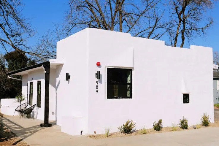 A white, modern, minimalist building with a small patio and address numbers 989.
