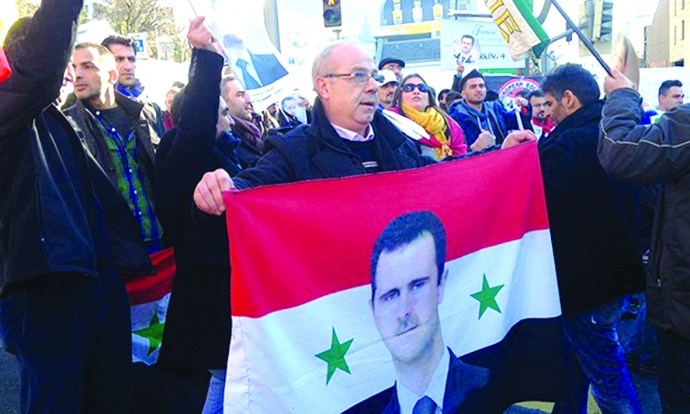 Một người ủng hộ giơ cao cờ Syria có mang hình Tổn