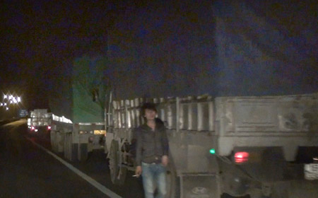 Đoàn xe tải nối đuôi chờ tín hiệu để vượt trạm (ảnh lớn); Một đối tượng cò đang hướng dẫn xe quá tải vào KCN để lách trạm cân (ảnh nhỏ) (Ảnh cắt từ clip)
