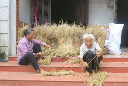Hai chị em cựu TNXP đơn thân Nguyễn Thị Lụa và Nguyễn Thị Lược ngồi đan chổi trước thềm nhà