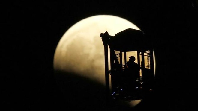 Một người đàn ông và một phụ nữ trên vòng quay Ferris tại thành phố Tokyo, Nhật Bản ngắm trăng khi nguyệt thực toàn phần bắt đầu vào tối 8/10. Ảnh: Reuters