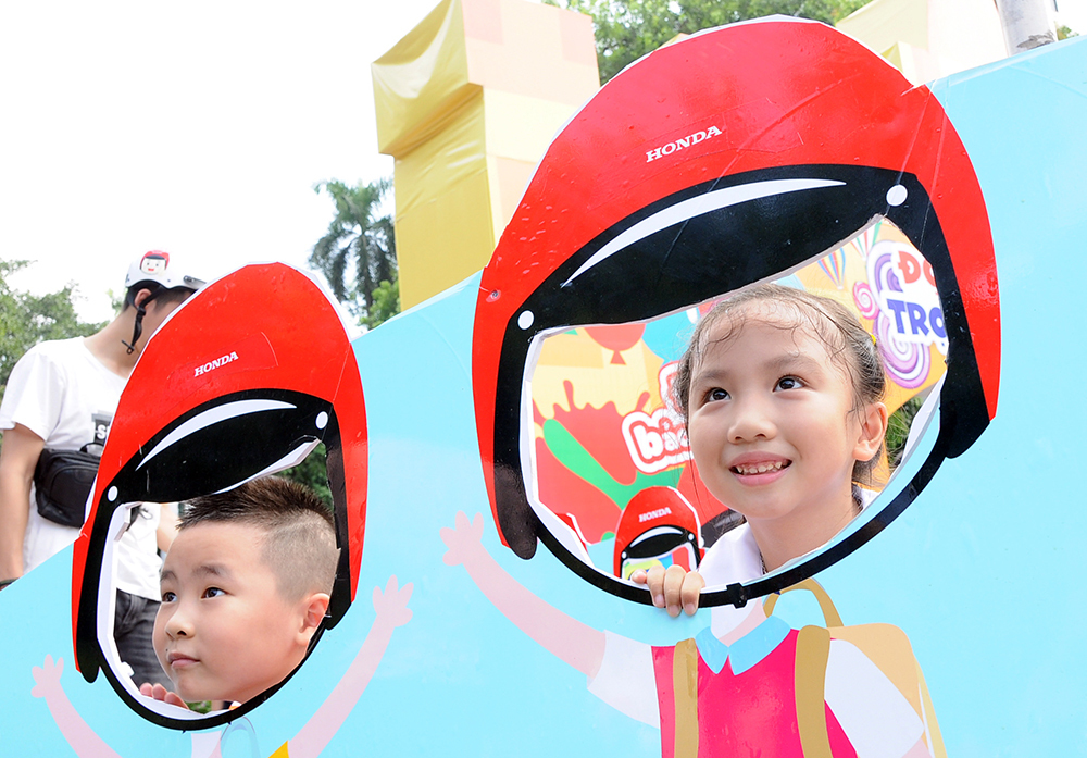 Các em nhỏ thích thú chụp ảnh với thông điệp luôn đội mũ bảo hiểm khi tham gia giao thông.