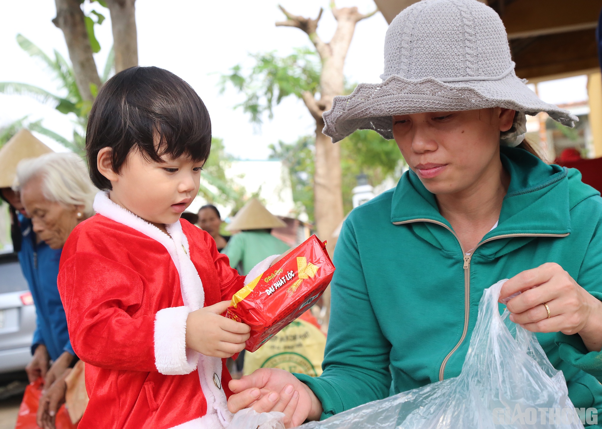 Bé Bùi Ngọc Nhã Quyên (3 tuổi, ở thôn Đông 2, xã Hiền Ninh) được mẹ cho gói bánh được lấy ra từ túi quà của Báo Giao thông và các nhà tài trợ.