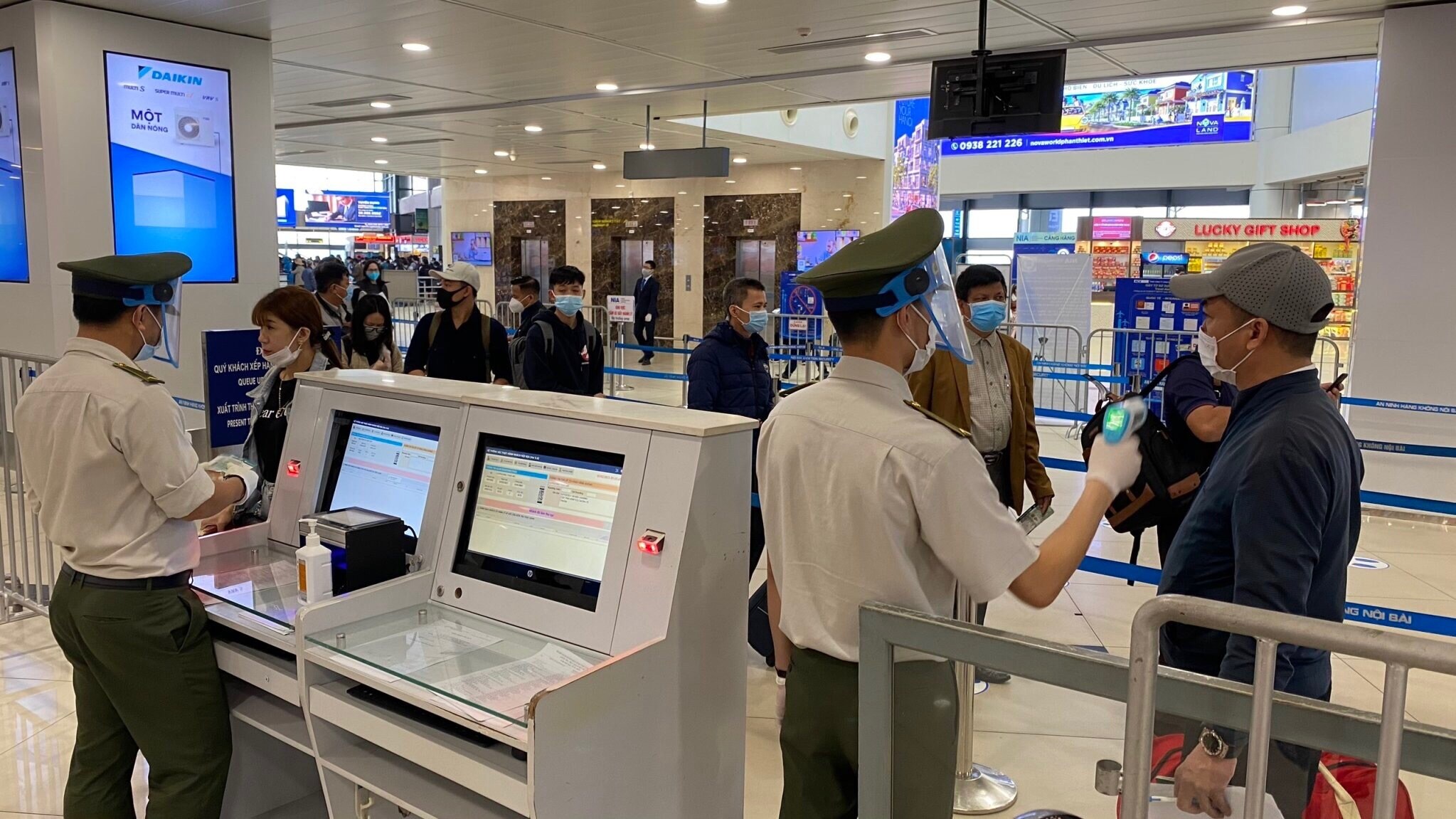 Nhân viên ANHK đo thân nhiệt cho hành khách. Lực lượng An ninh hàng không Nội Bài được trang bị đầy đủ găng tay, khẩu trang, tấm chắn giọt bắn trong khi làm việc.