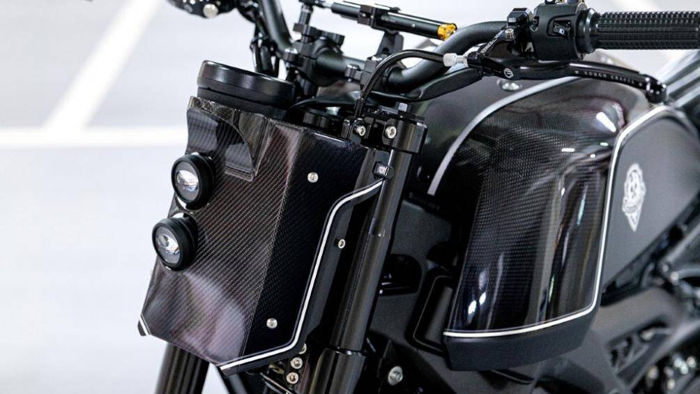 Phía trước đầu xe, cụm đèn pha tròn nguyên bản được thay thế bằng hai bóng projector nằm trên tấm bảng số làm từ sợi carbon