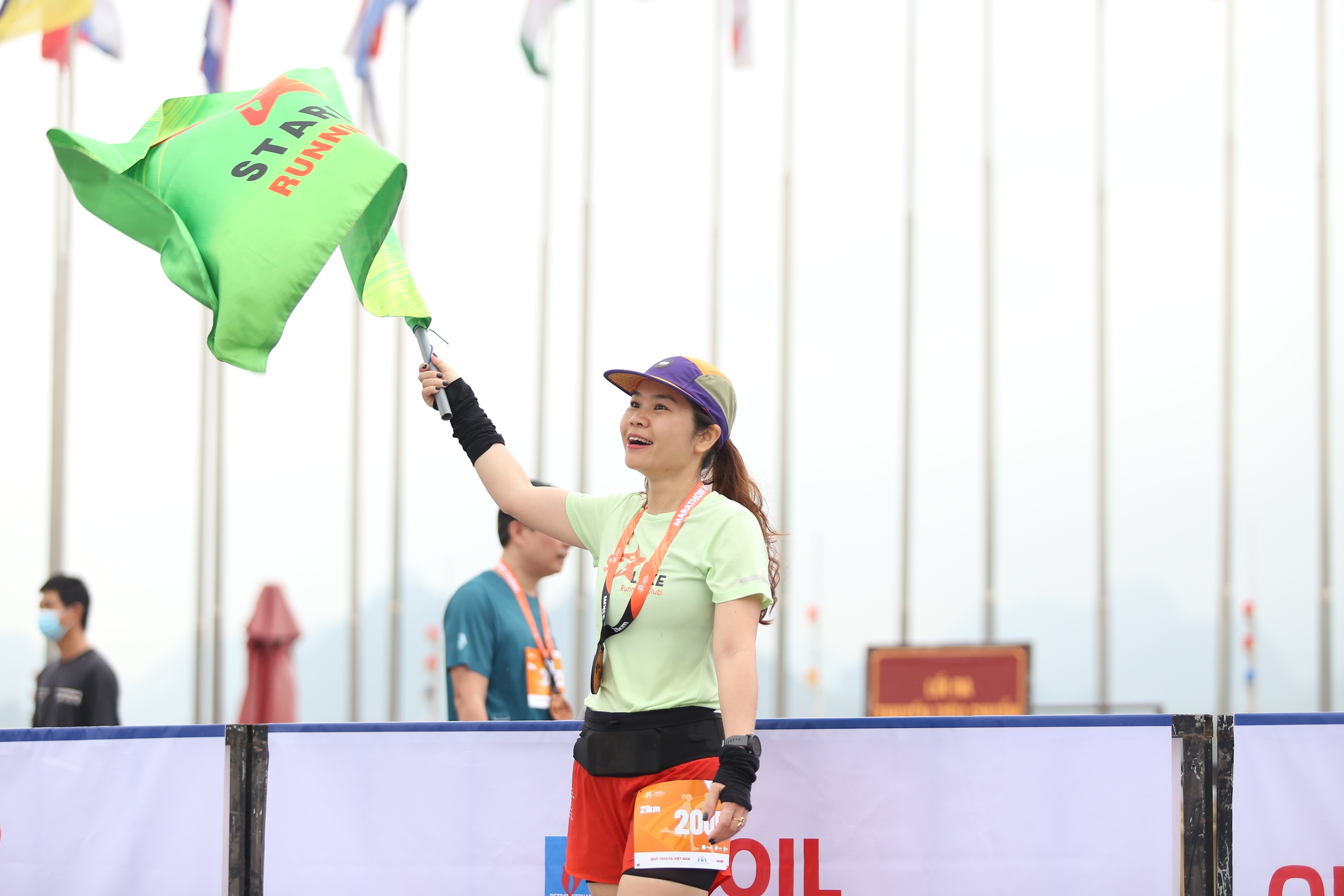 Một vận động viên về đích trước vẫy cờ chào đón những người hoàn thành quãng đường chạy sau mình.