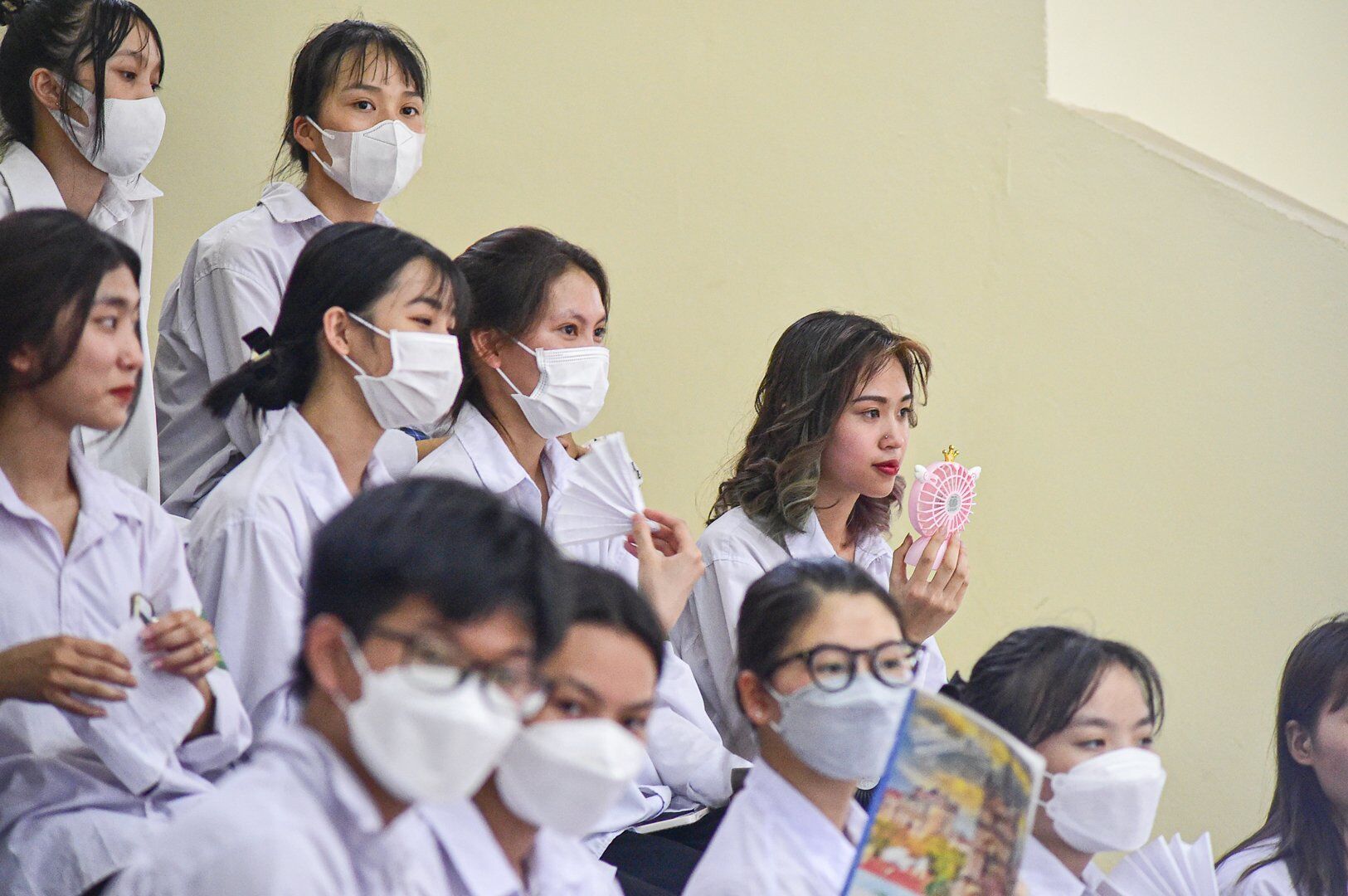Do trời nóng, điều hòa trong Nhà thi đấu không đủ làm mát không khí nên nhiều em dùng quạt mini hoặc vở để quạt.