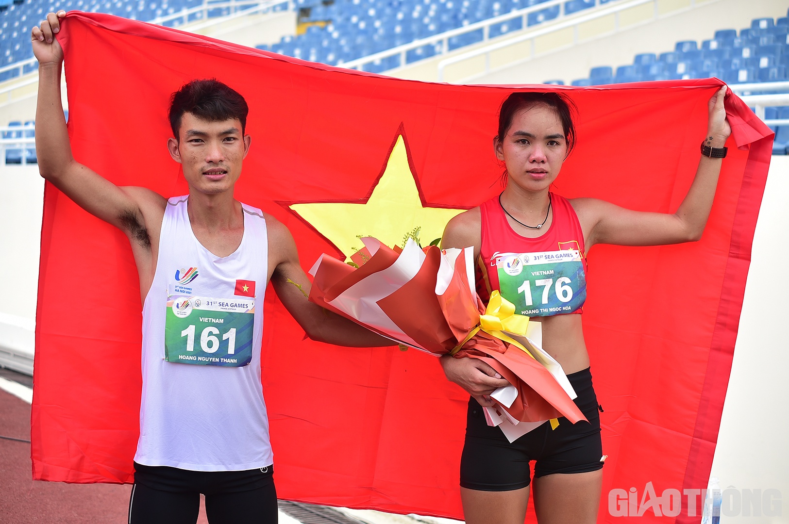 Hoàng Nguyên Thanh, nhà vô địch nội dung marathon nam, ôm hoa đến tặng và khoác cờ Tổ quốc động viên Hoàng Thị Ngọc Hoa. Cả 2 đều là các VĐV của Bình Phước, cùng vô địch Tiền Phong marathon 2022 trước khi tham dự SEA Games 31.