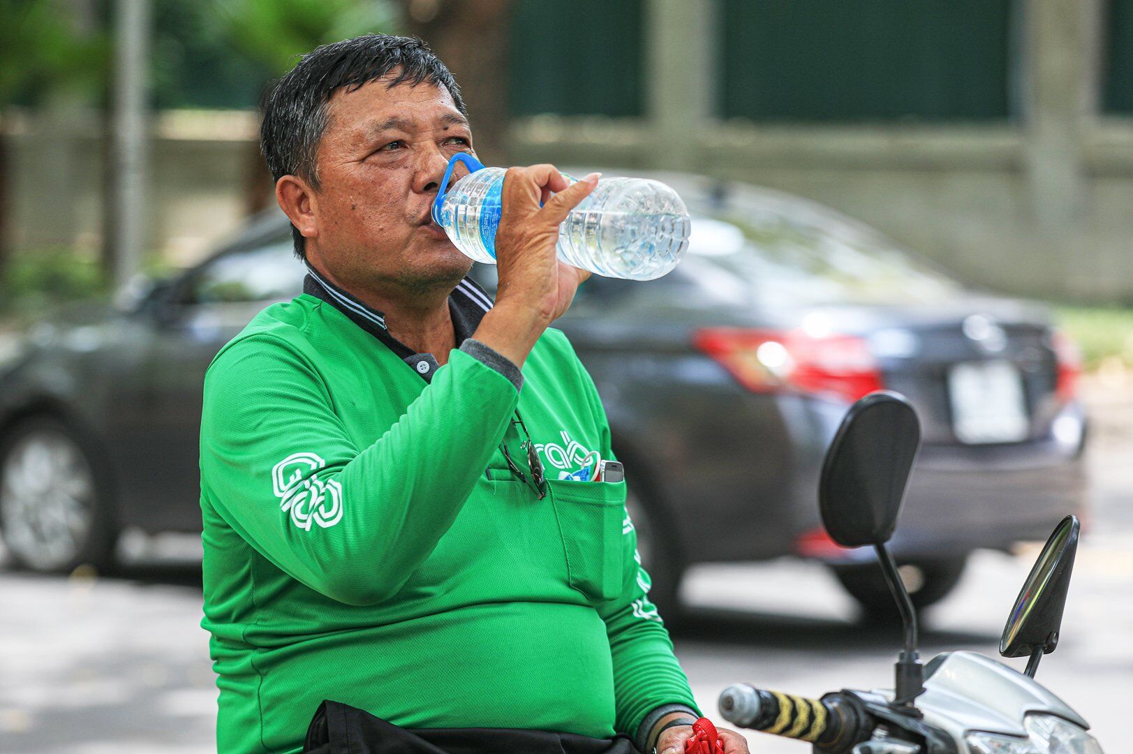 Để chống chọi với nắng nóng, tài xế xe ôm này phải liên tục uống nước.