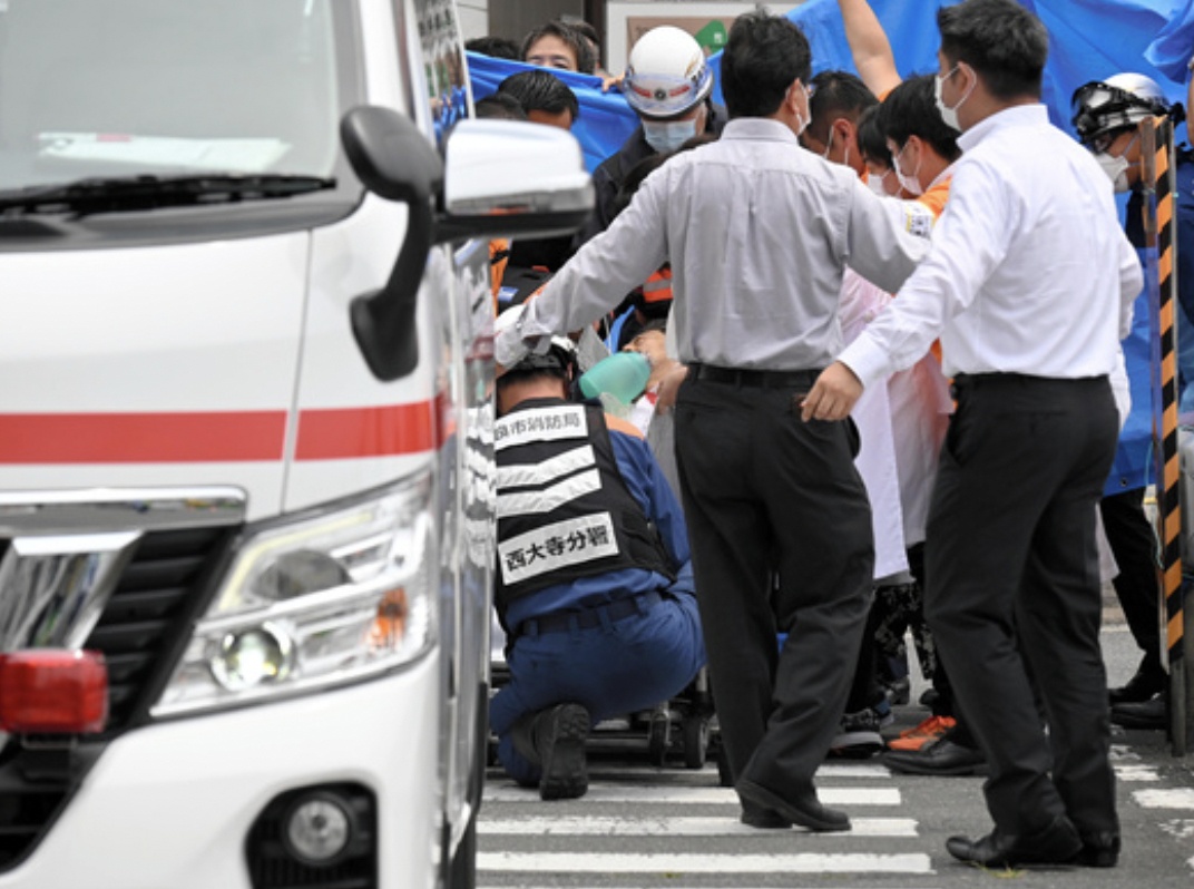 Lực lượng cứu hộ dùng bạt che chắn trong lúc nhân viên y tế sơ cứu cho ông Abe. Ảnh - Asahi