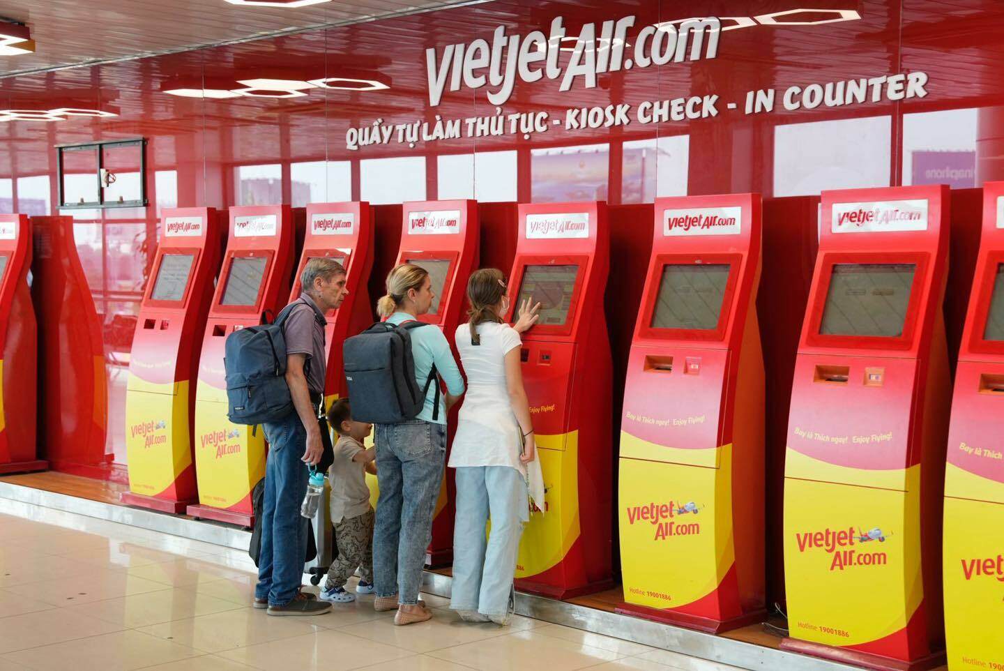 Một nhóm gia đình người nước ngoài tự làm thủ tục check in tại các kiosk của hãng Vietjet Air.