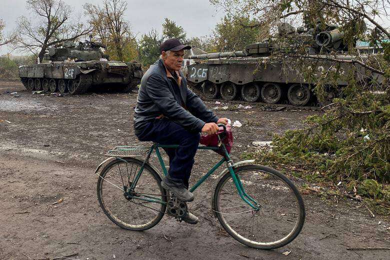 Người dân địa phương đi xe đạp ngang qua xác xe tăng mà Nga bỏ lại tại làng Kurylivka, khu vực Kharkiv, Ukraine. Ảnh - Reuters