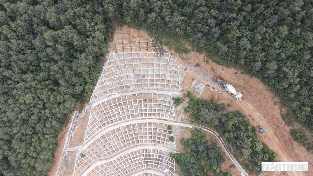 Ở bên ngoài, các công nhân đang gia cố đỉnh mái ta luy. Họ phải làm việc ở địa hình dốc hiểm trở, ở độ cao hơn 100m so với nền đường.