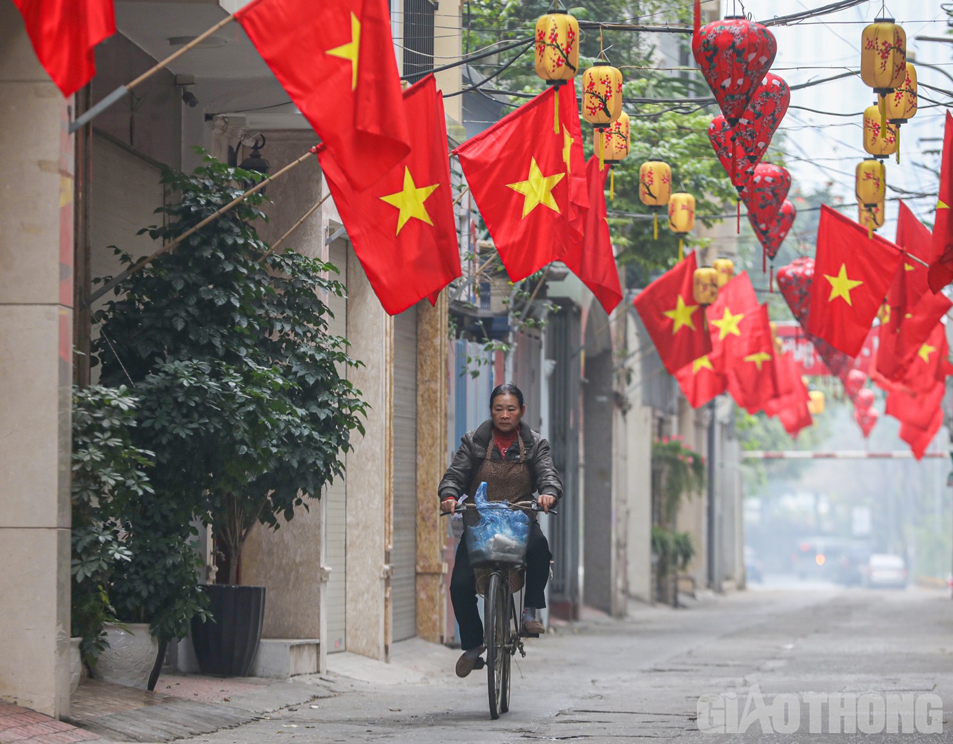 Người phụ nữ đạp xe bán muối đầu năm trong con ngõ nhỏ nổi bật với cờ đỏ sao vàng.