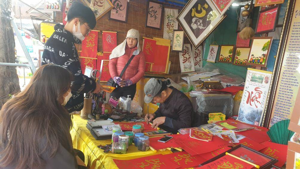 Những bạn trẻ chăm chú, háo hức xem một nghệ nhân viết chữ thư pháp.