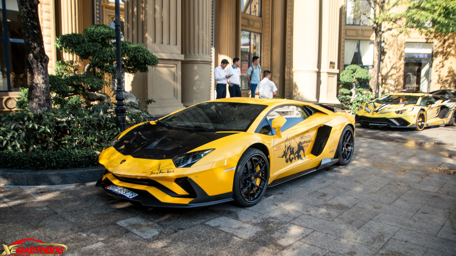 Lamborghini Aventador LP700-4 với gói độ thân rộng đến từ Duke Dynamics (phía sau). Xe được trang bị nhiều chi tiết bằng carbon như cản trước pha trộn giữa Aventador SV và SVJ, các khe gió trên vòm bánh xe được mở rộng, ốp sườn. Ở phía sau có bộ khuếch tán chia thành 3 phần riêng biệt lấy cảm hứng từ siêu xe giới hạn Lamborghini Centenario và cánh gió cỡ lớn