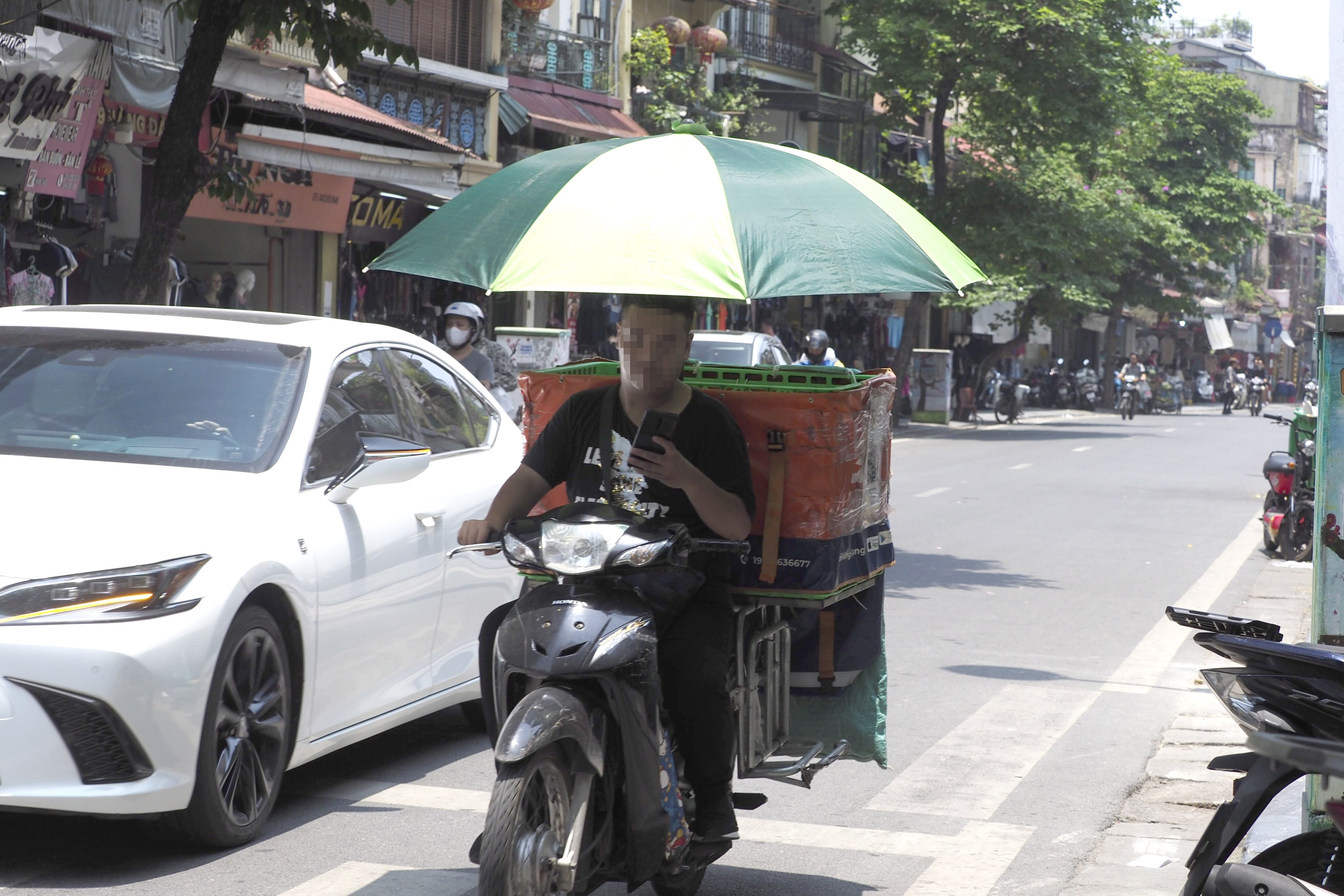 Người đàn ông làm nghề shipper này đã sử dụng chiếc ô để chống chọi với cái nắng đầu mùa.