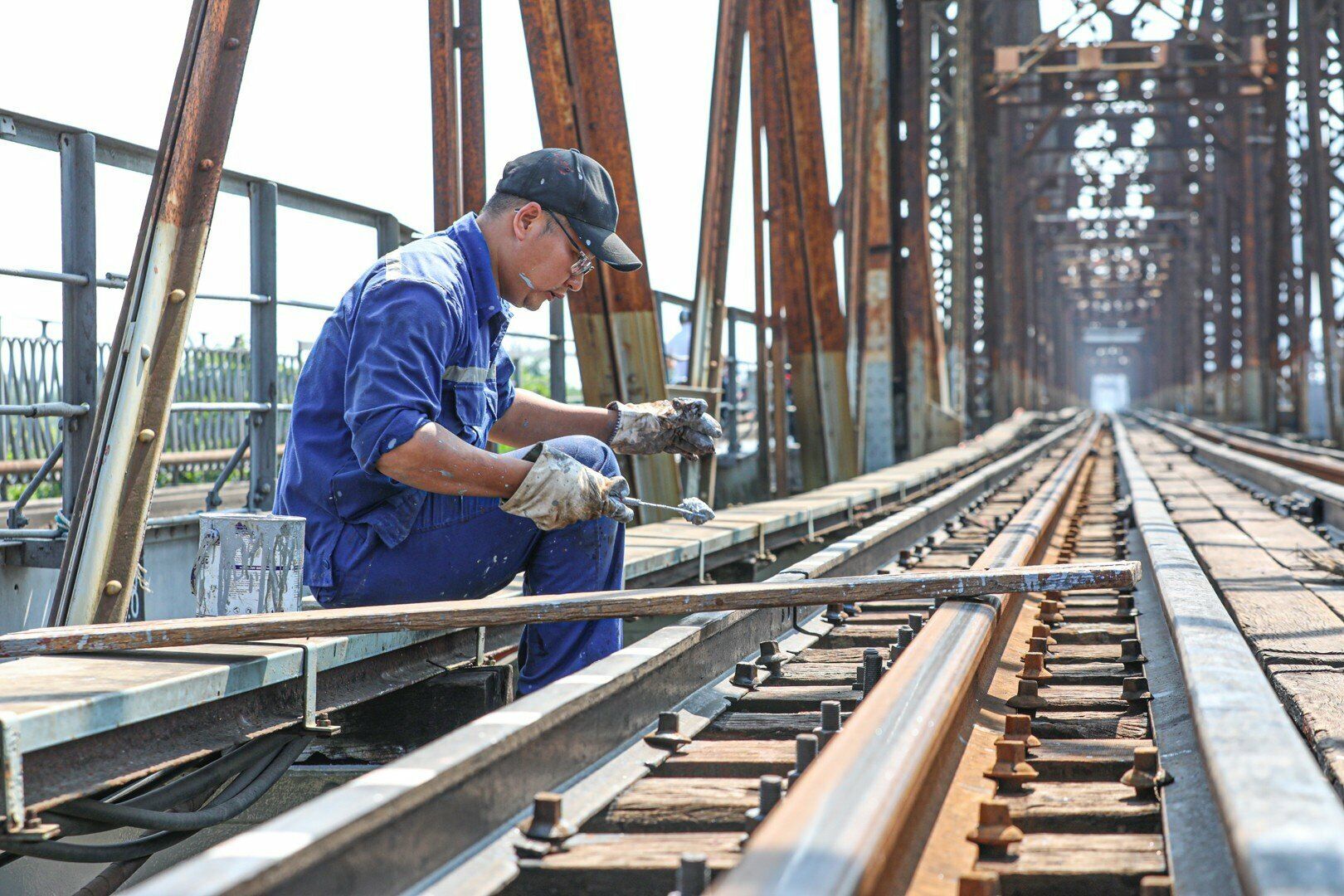 Anh Thuỷ (Đội quản lý cầu Long Biên, Công ty CP Đường sắt Hà Hải) vừa mải mê sơn các tấm thép vừa cho biết, nhóm anh đang thực hiện công việc duy tu thường xuyên. Trong đó, hạng mục sơn cầu không chỉ là tân trang, làm đẹp cầu mà quan trọng là thêm biện pháp chống xuống cấp, đảm bảo an toàn. Vì phải qua nhiều công đoạn như cạo rỉ, đánh sạch lớp sơn cũ, các rỉ sét, sơn chống rỉ rồi mới sơn phủ. “Đây là công việc thường ngày thôi, để duy tu cầu cho đảm bảo an toàn nên nắng vẫn làm, để còn nhanh hoàn thành”, anh Thuỷ nói.