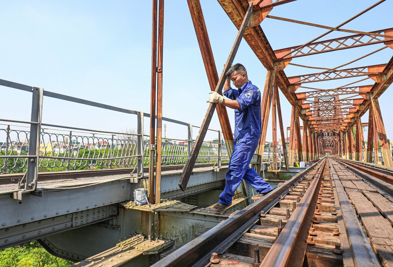 Anh Hiệp, người cùng nhóm sản xuất với anh Thuỷ cho hay, để vẫn hoàn thành công việc, đồng thời tránh bớt nắng nóng, các anh làm từ 6h00 sáng. Mỗi nhóm được giao khoán phụ trách một đoạn, cứ thế các nhóm tập trung sơn, làm đến tận trưa, đến khi nào hoàn thành mới thôi. Ảnh: Anh Thuỷ chuẩn bị các thanh gá trước khi vào vị trí sơn phía dưới mặt cầu