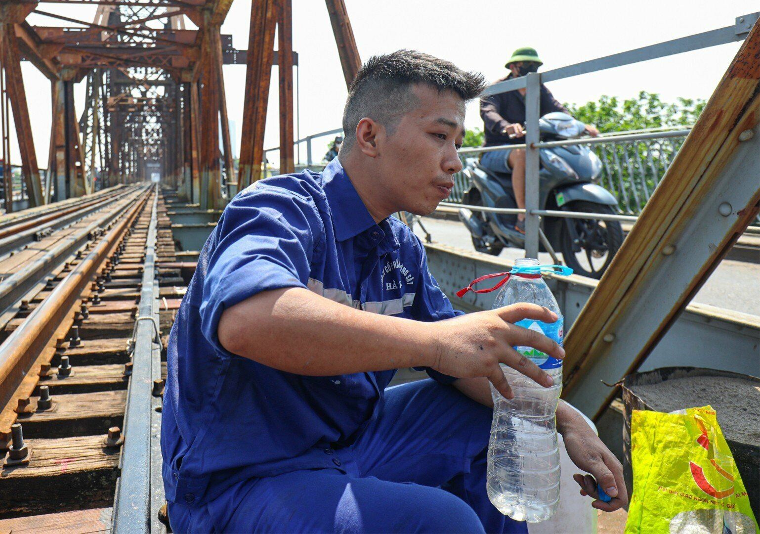 Công nhân đường sắt tranh thủ làm nhanh cho sớm hoàn thành công việc nên phút nghỉ ngơi rất hiếm hoi, chóng vánh. Ảnh: Anh Hiệp tranh thủ vừa pha sơn, vừa uống nước trước khi vào vị trí sơn mới