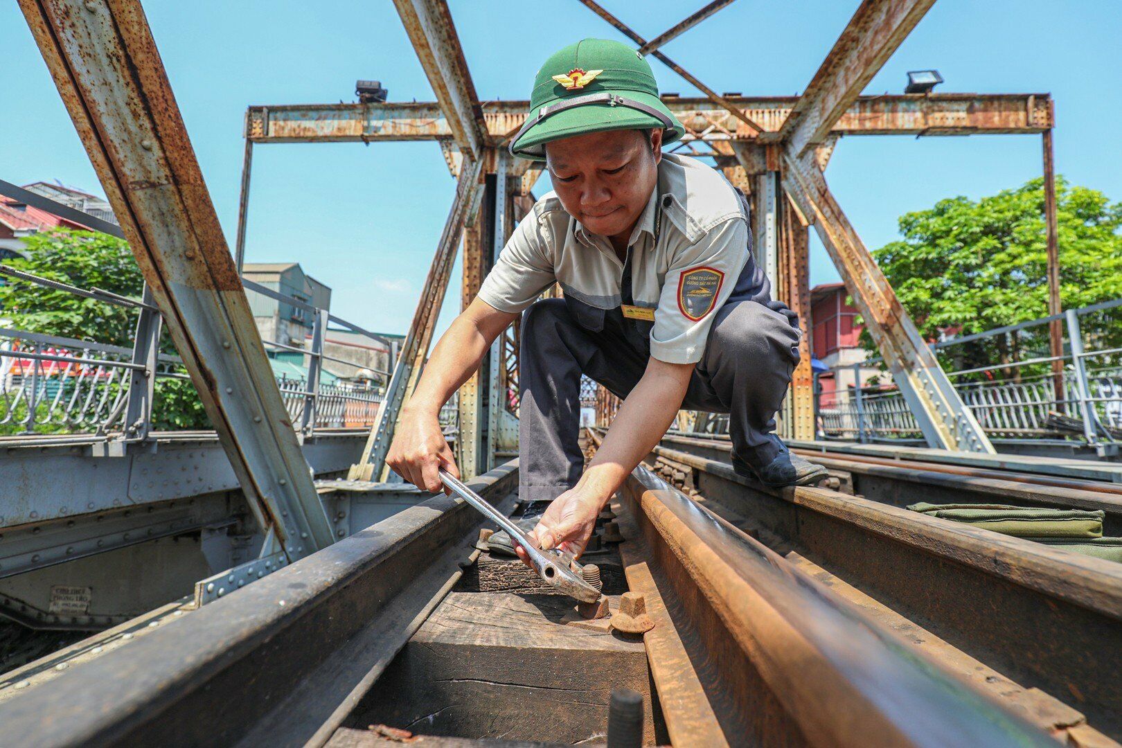 Tham gia bảo đảm an toàn cho cầu Long Biên còn lực lượng tuần gác. Anh Đào Minh Dực, công nhân tuần cầu cho biết, anh đã làm công nhân tuần cầu trên 10 năm. Hàng ngày, sau khi nhận ban lúc 6h, anh phải đi tuần dọc theo đường sắt trên cầu, vừa đi vừa quan sát đường sắt và cả đường bộ xem có xảy ra vấn đề gì uy hiếp đến an toàn không để xử lý kịp thời. Ảnh: Anh Dực siết lại bu lông giữ tà vẹt bị lỏng giữa nắng gắt