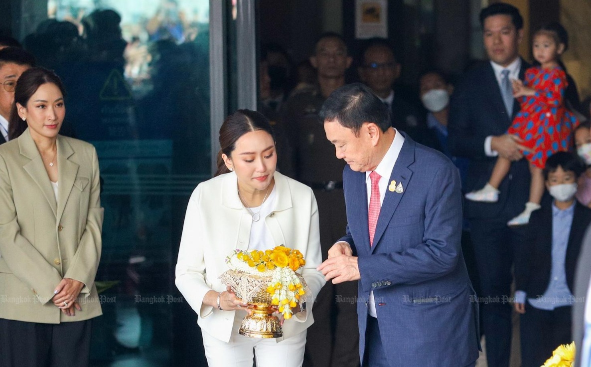 Ông Thaksin mặc bộ comple màu xanh đậm, đeo cà vạt màu hồng đi ra ngoài cửa nhà ga dành cho máy bay riêng cùng ba con Panthongtae, Pintongta và Paetongtarn.